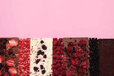 Different chocolate bars with freeze dried fruits on pink background, flat lay. Space for text