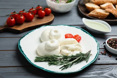Photo of Delicious burrata cheese with rosemary and cut tomato served on grey wooden table