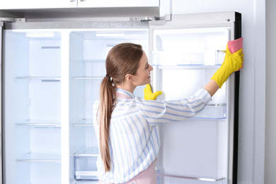 Woman in rubber gloves cleaning refrigerator at home