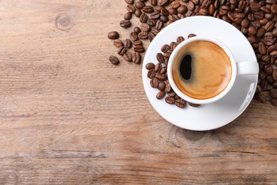 Photo of Cup of hot aromatic coffee and roasted beans on wooden table, flat lay. Space for text