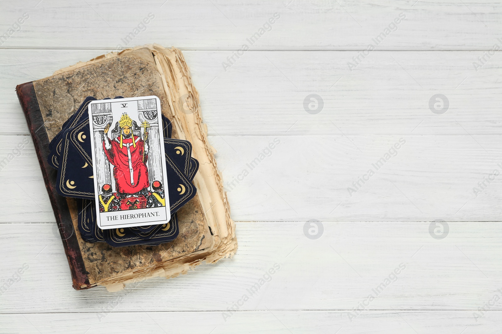 Photo of The Hierophant and other tarot cards with old book on white wooden table, top view. Space for text