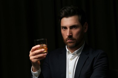 Handsome man in suit holding glass of whiskey on black background