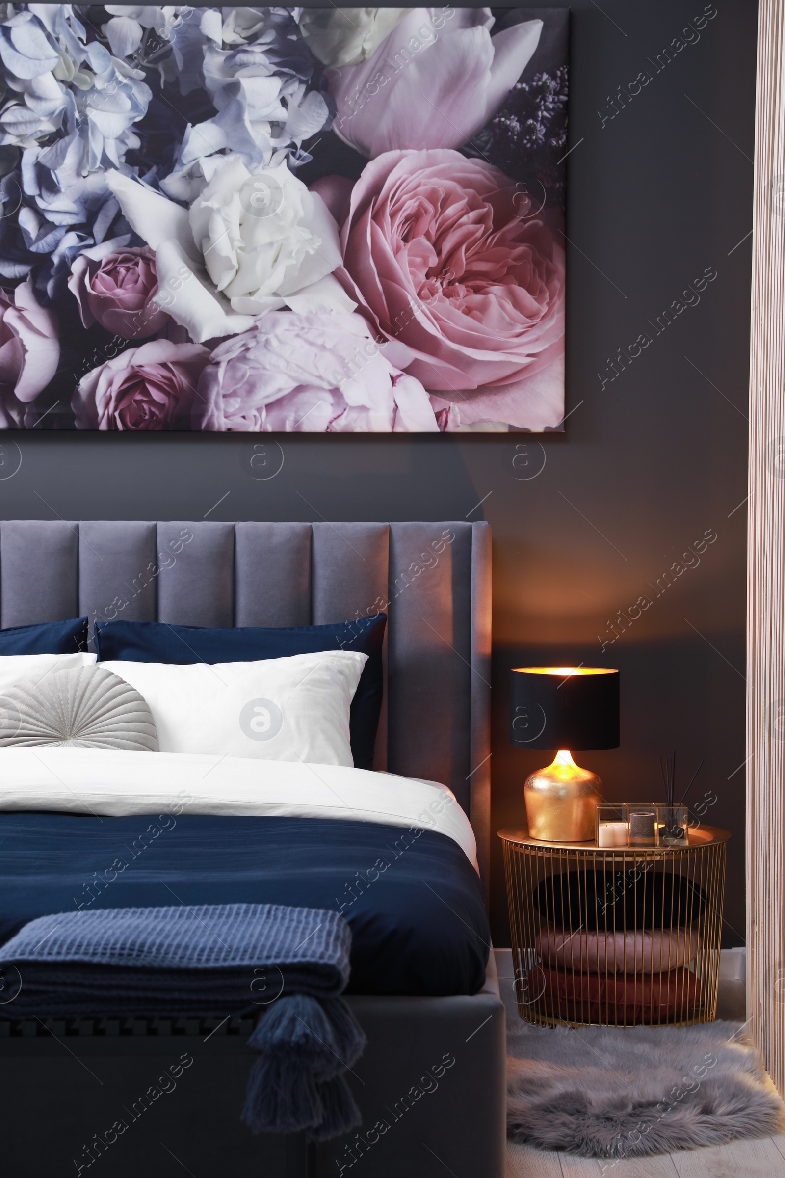 Photo of Comfortable bed with cushions, lamp and different decor on bedside table in room. Stylish interior