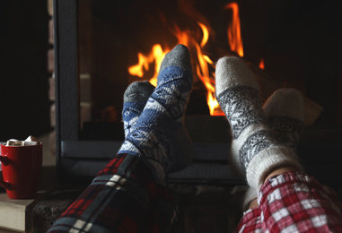 Photo of Couple in pajamas resting near fireplace indoors, closeup. Winter vacation