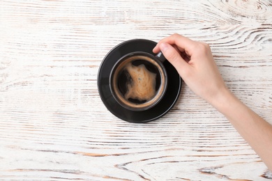 Young woman with cup of delicious hot coffee on wooden background, top view