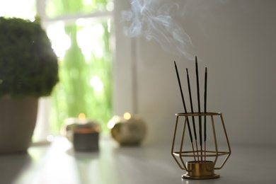 Photo of Incense sticks smoldering on table in room. Space for text