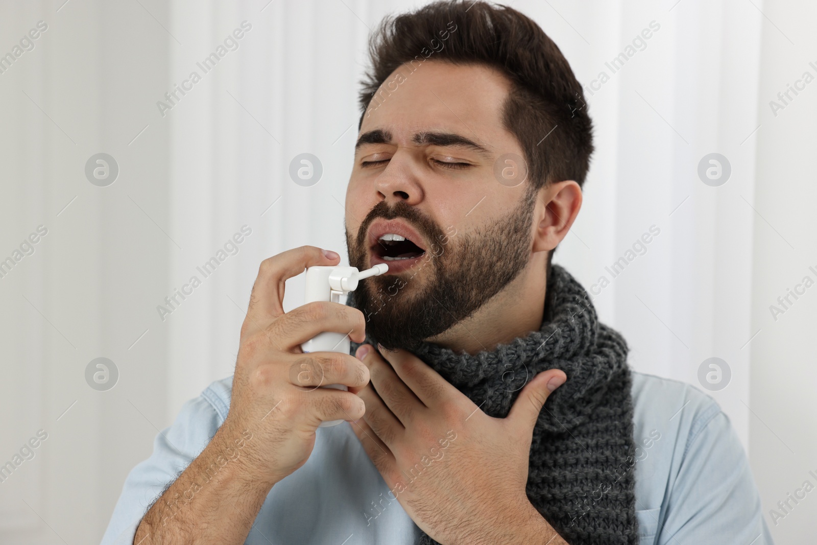 Photo of Young man with scarf using throat spray indoors