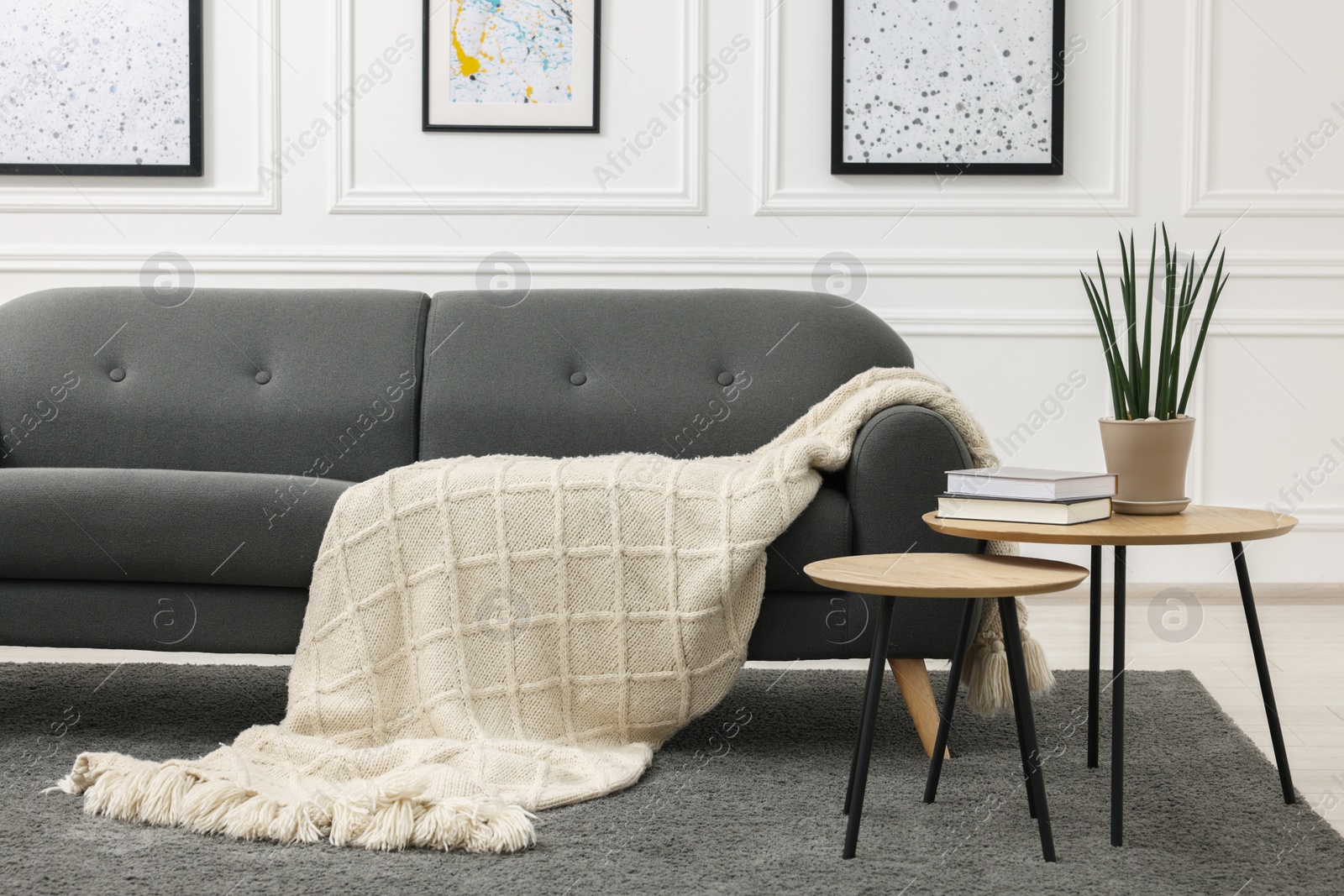 Photo of Stylish living room interior with comfortable sofa, blanket and nesting tables