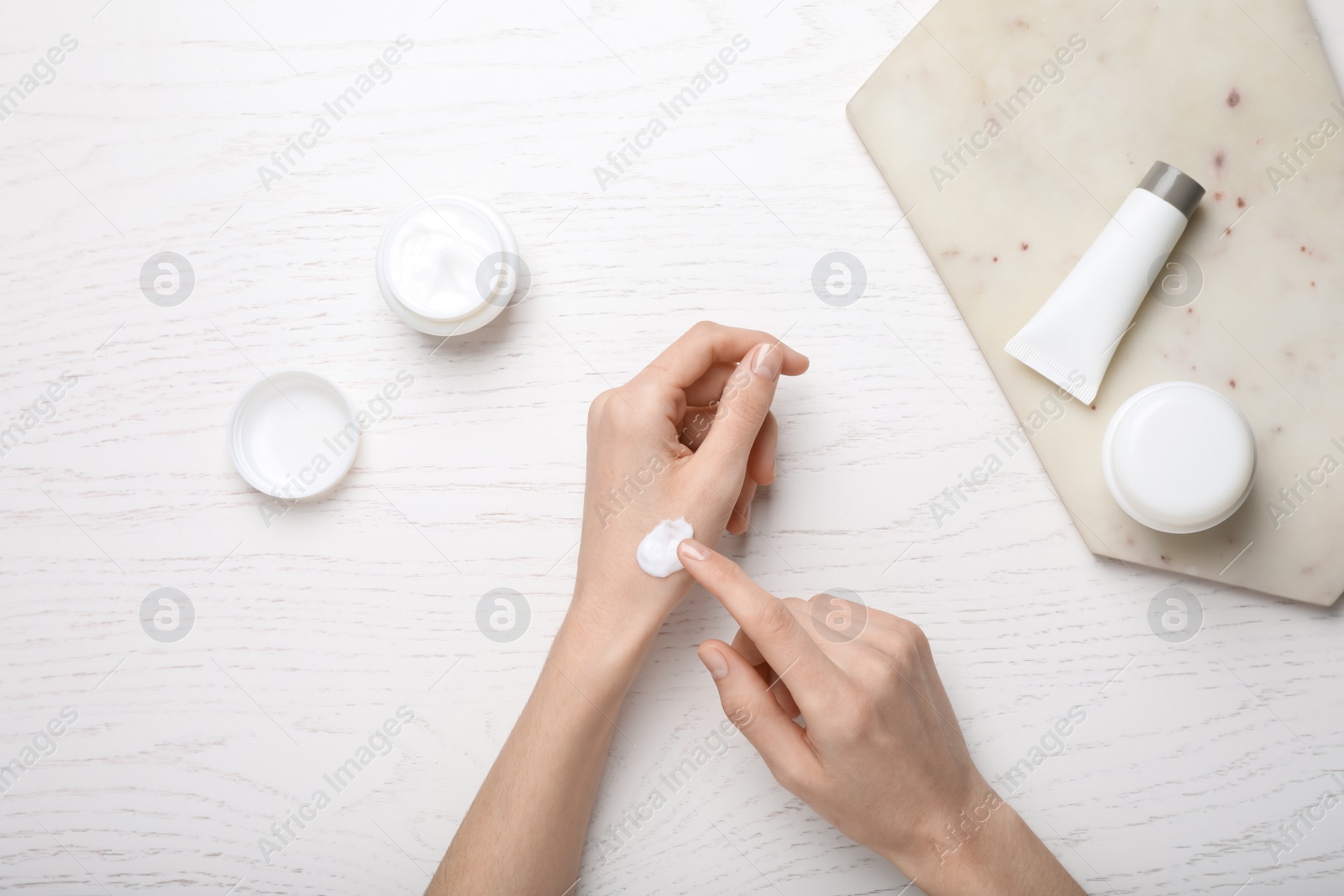 Photo of Woman applying body cream onto her wrist at white wooden table, top view