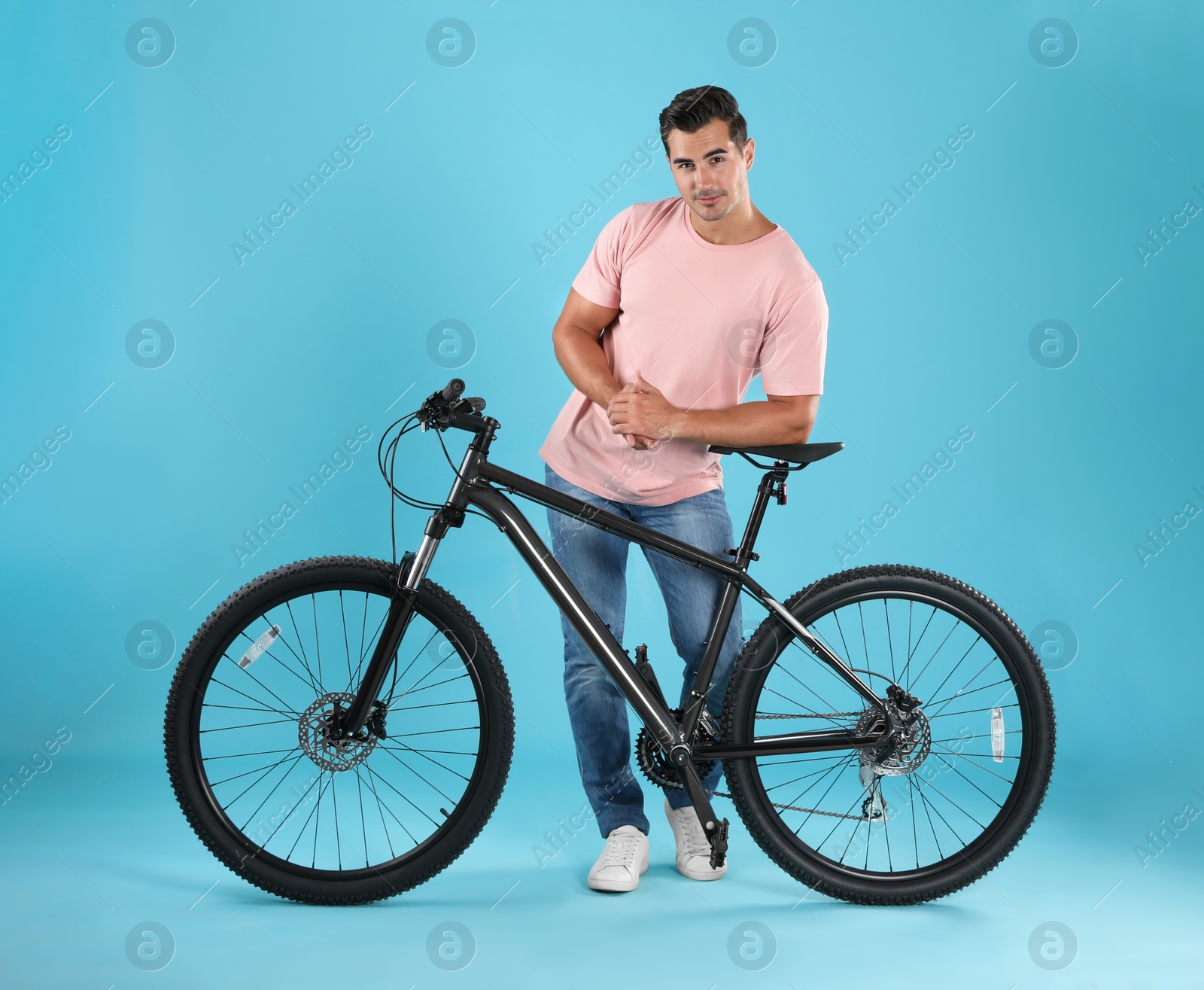 Photo of Handsome young man with modern bicycle on light blue background