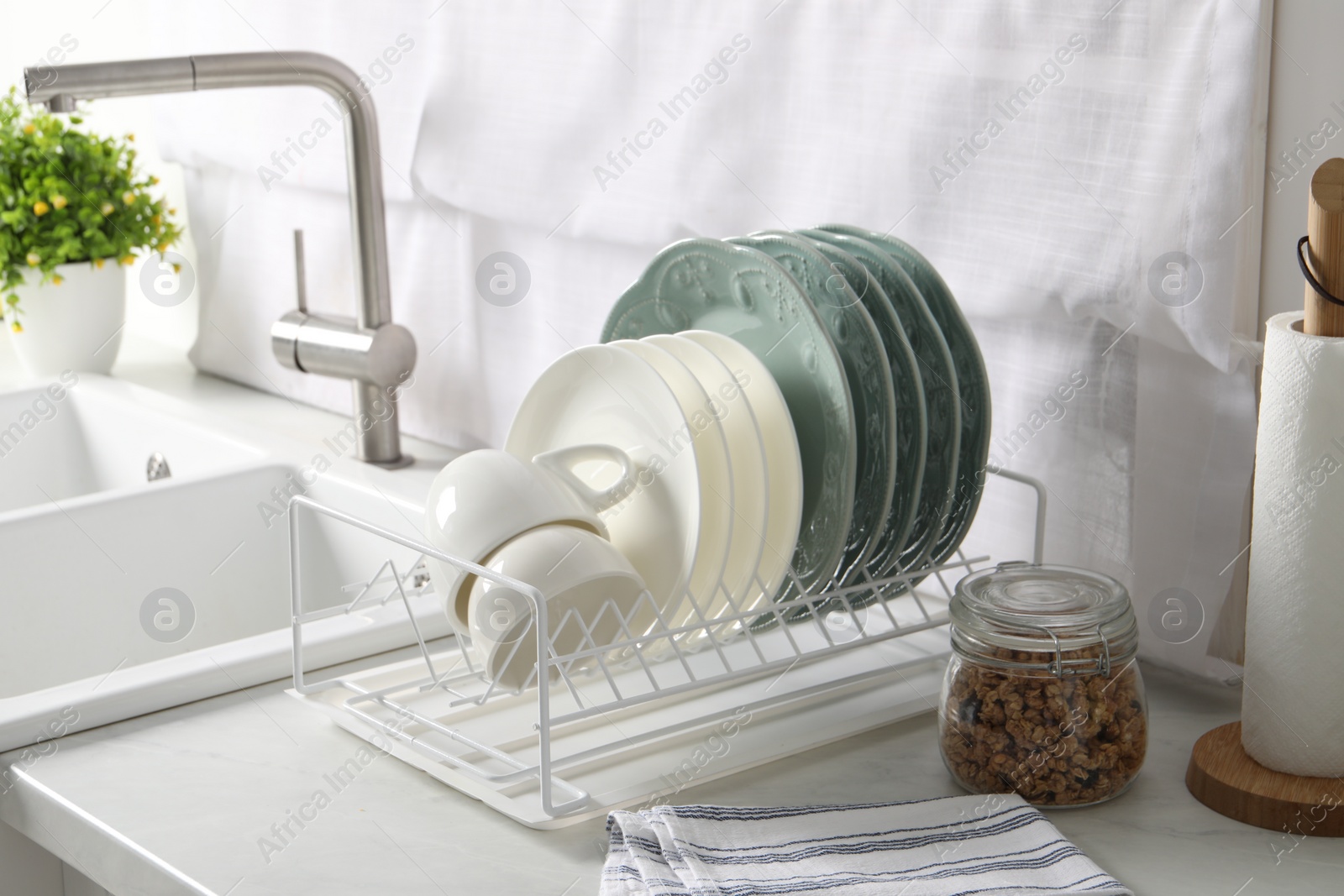 Photo of Drainer with different clean dishware and cups on white table in kitchen