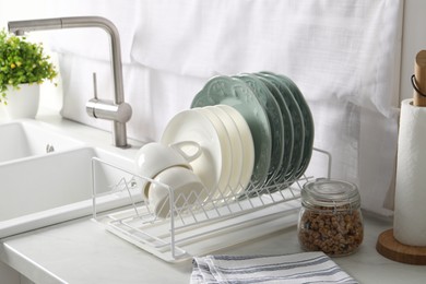Photo of Drainer with different clean dishware and cups on white table in kitchen