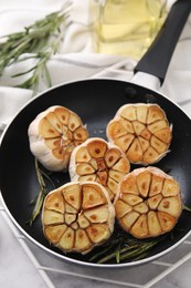 Photo of Frying pan with fried garlic and rosemary on table