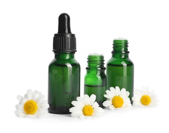 Photo of Chamomile flowers and cosmetic bottles of essential oil on white background