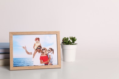 Photo of Frame with family photo and green houseplant on white table, space for text