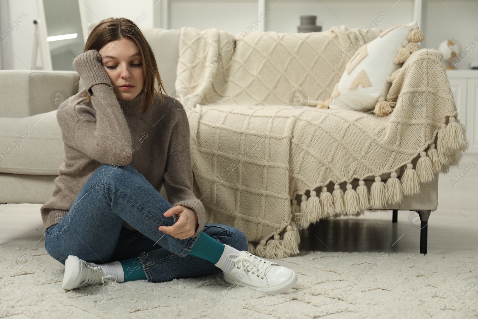 Photo of Sad young woman sitting on floor at home, space for text