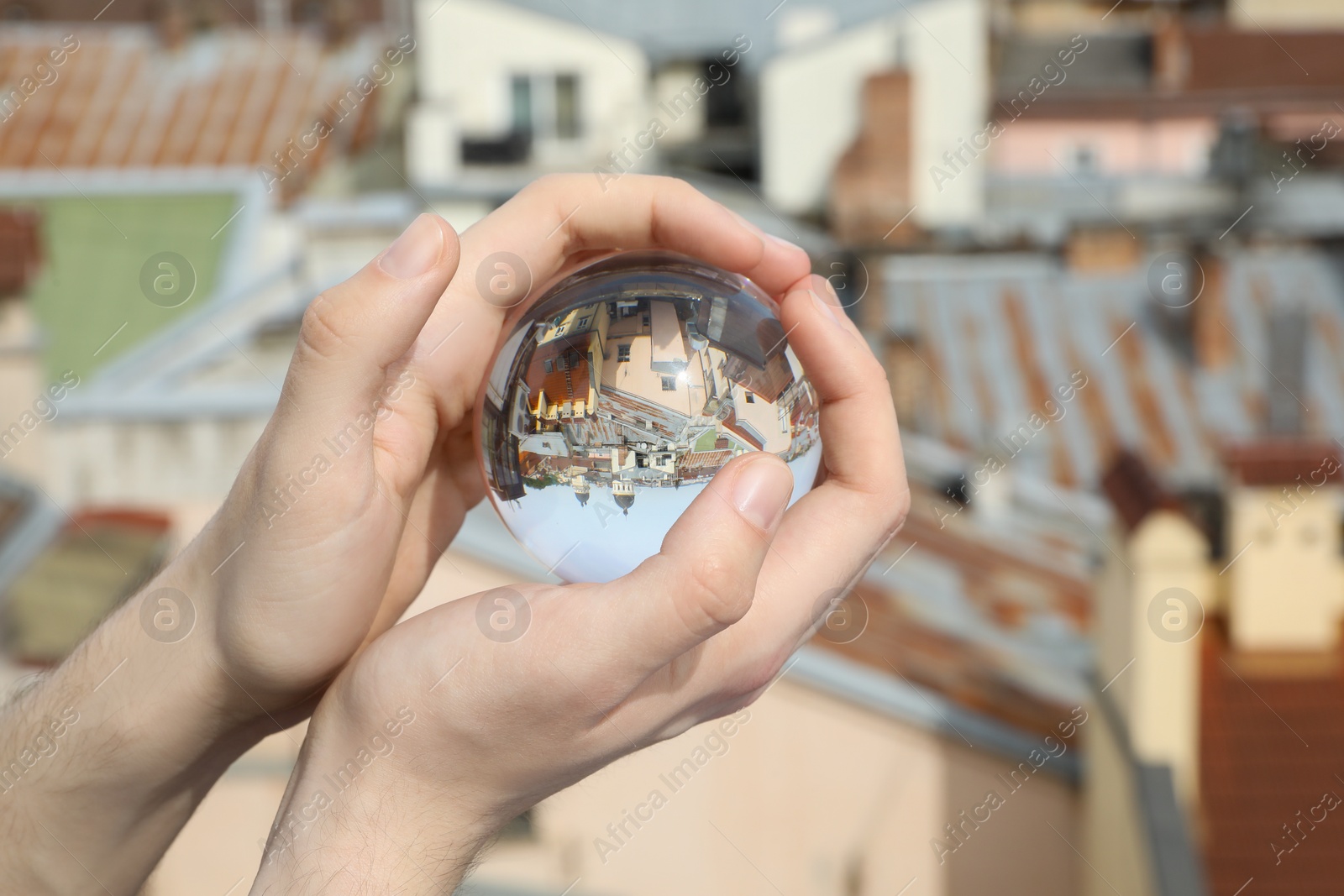 Photo of View of beautiful city street, overturned reflection. Man holding crystal ball outdoors, closeup