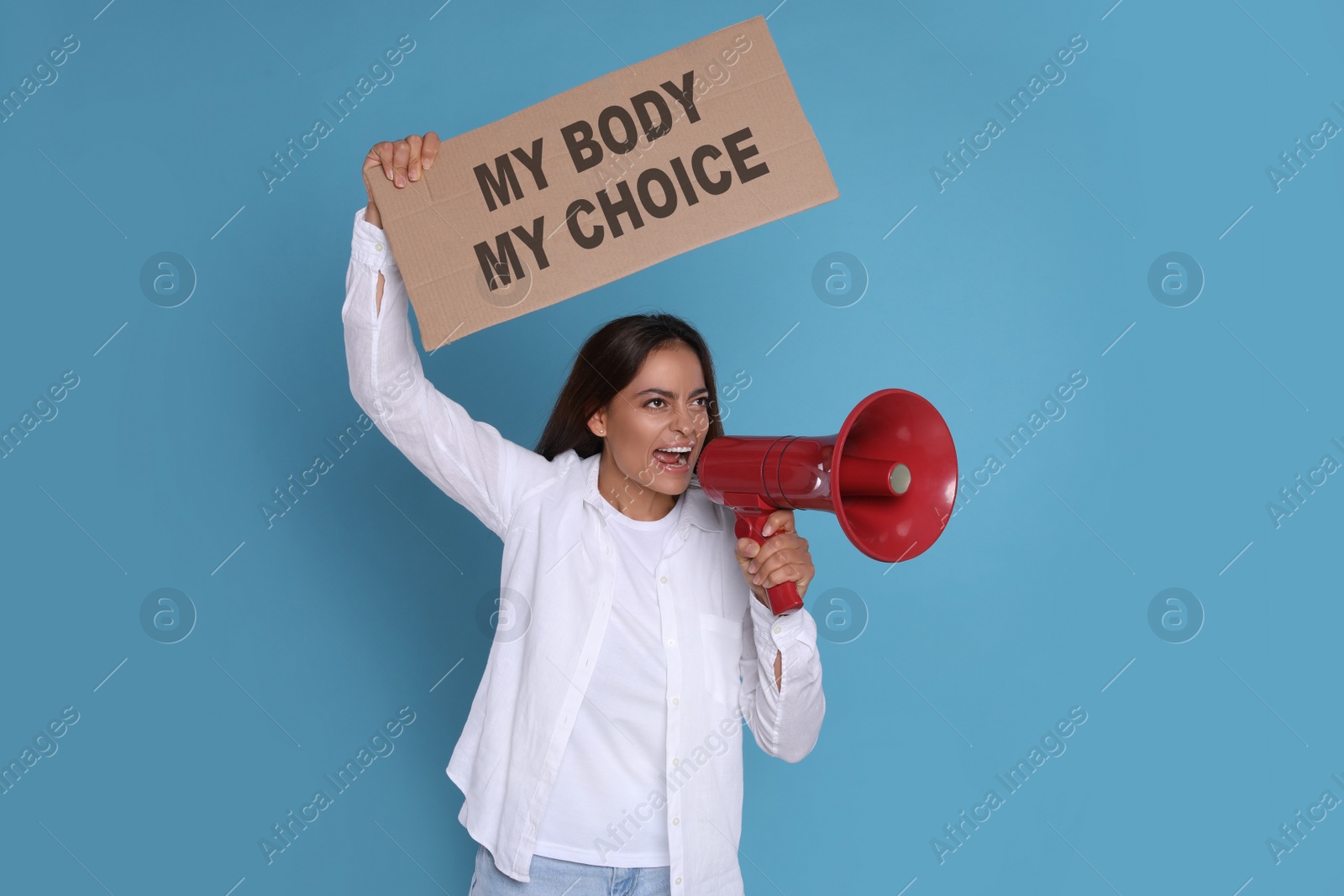 Image of Emotional woman shouting into megaphone and holding placard with phrase My Body My Choice on light blue background. Abortion protest