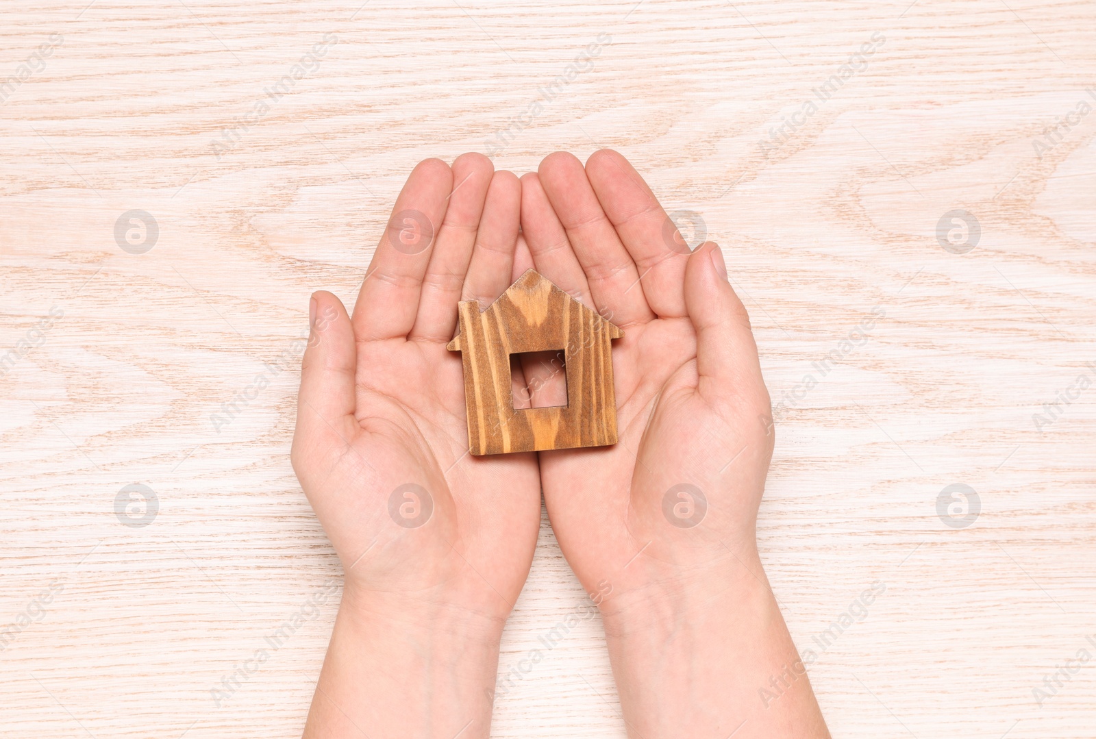 Photo of Home security concept. Man holding house model at wooden table, top view