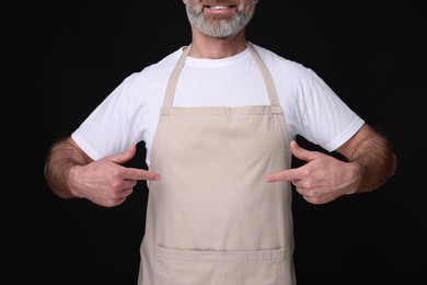 Photo of Man pointing at kitchen apron on black background, closeup. Mockup for design