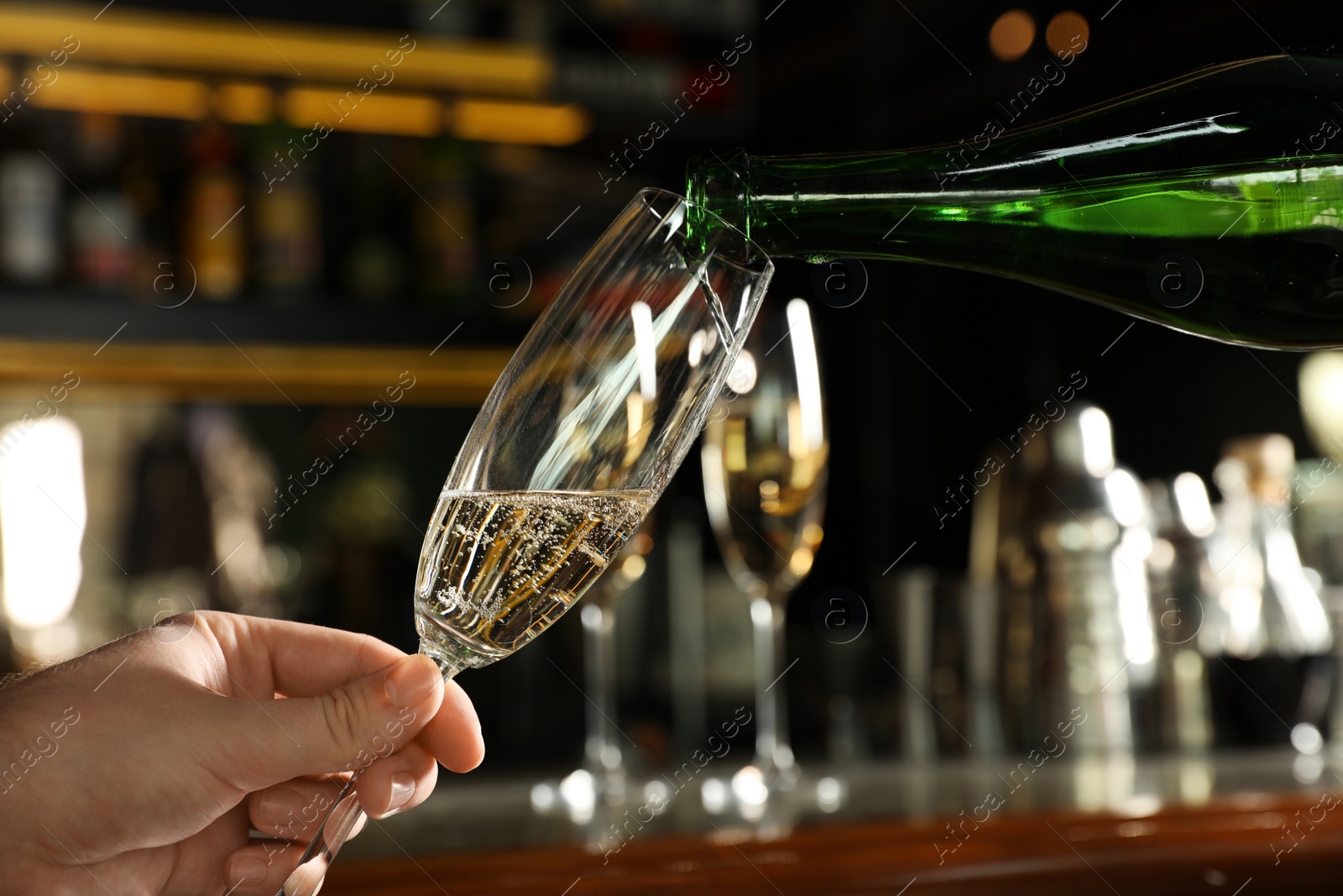 Photo of Pouring champagne from bottle into glass for man in bar, closeup