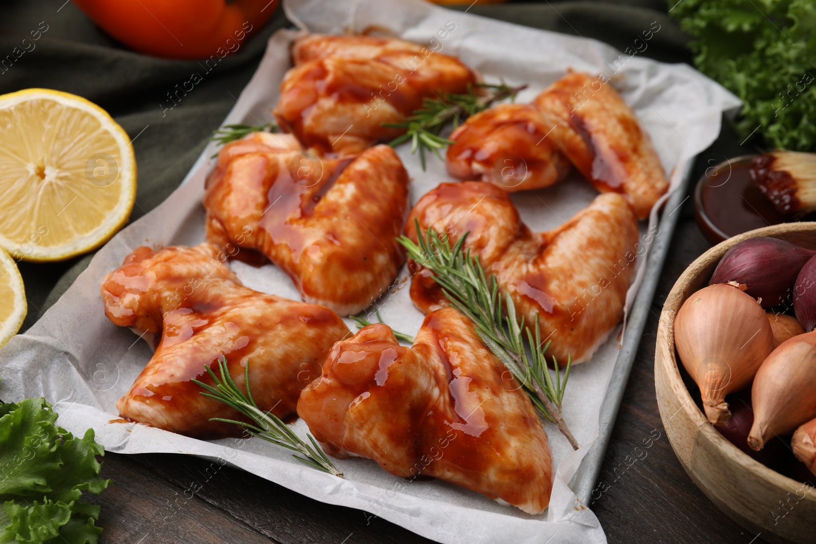 Photo of Raw marinated chicken wings, rosemary and other products on wooden table, closeup