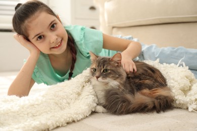 Cute little girl with cat lying on carpet at home. First pet