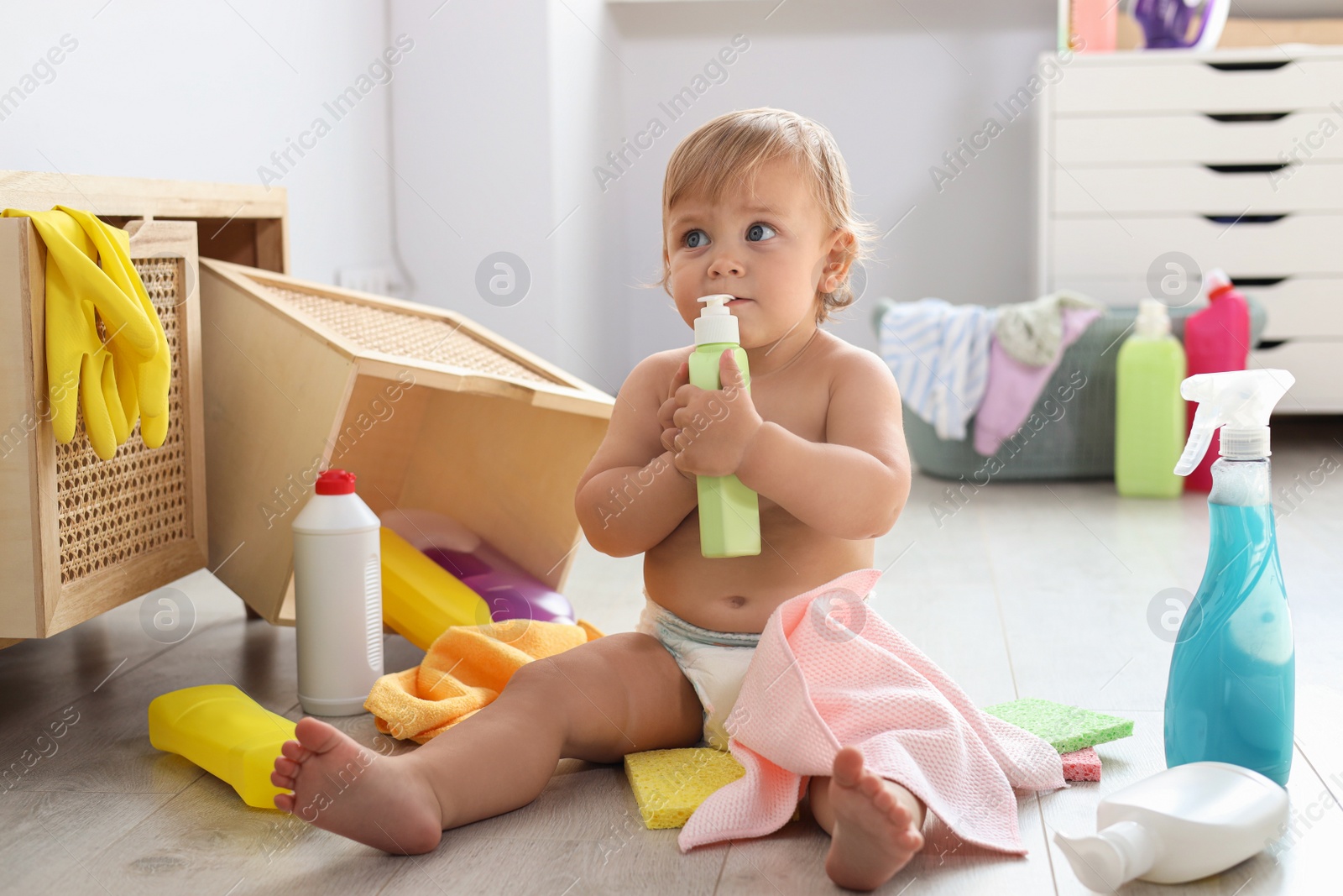 Photo of Cute baby playing with bottle of detergent on floor at home. Dangerous situation