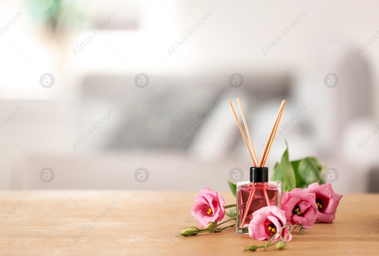 Photo of Aromatic reed air freshener and roses on table indoors