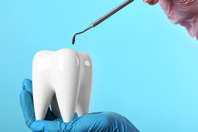 Dentist holding ceramic model of tooth and professional tool on color background, space for text