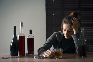 Photo of Alcohol addiction. Woman chained with glass of liquor at wooden table in room