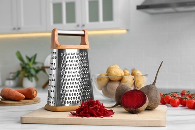 Photo of Grater and fresh ripe beetroots on white table in kitchen