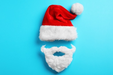 Santa Claus hat and beard on light blue background, flat lay