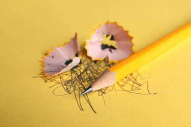 Photo of One sharp graphite pencil, scribbles and shavings on yellow background, closeup