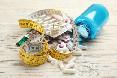 Photo of Many different weight loss pills and measuring tape on white wooden table