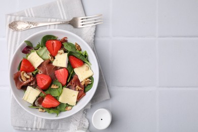 Photo of Tasty salad with brie cheese, prosciutto, strawberries and walnuts served on white tiled table, flat lay. Space for text