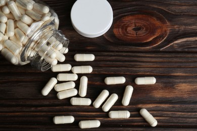 Glass medical bottle and pills on wooden table, flat lay