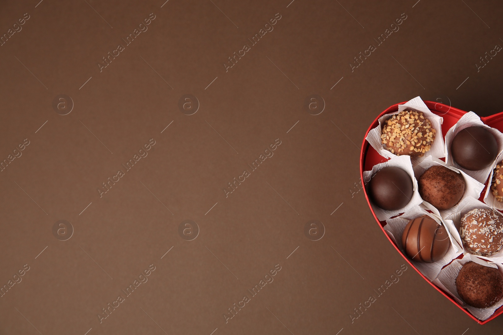 Photo of Heart shaped box with delicious chocolate candies on brown background, top view. Space for text