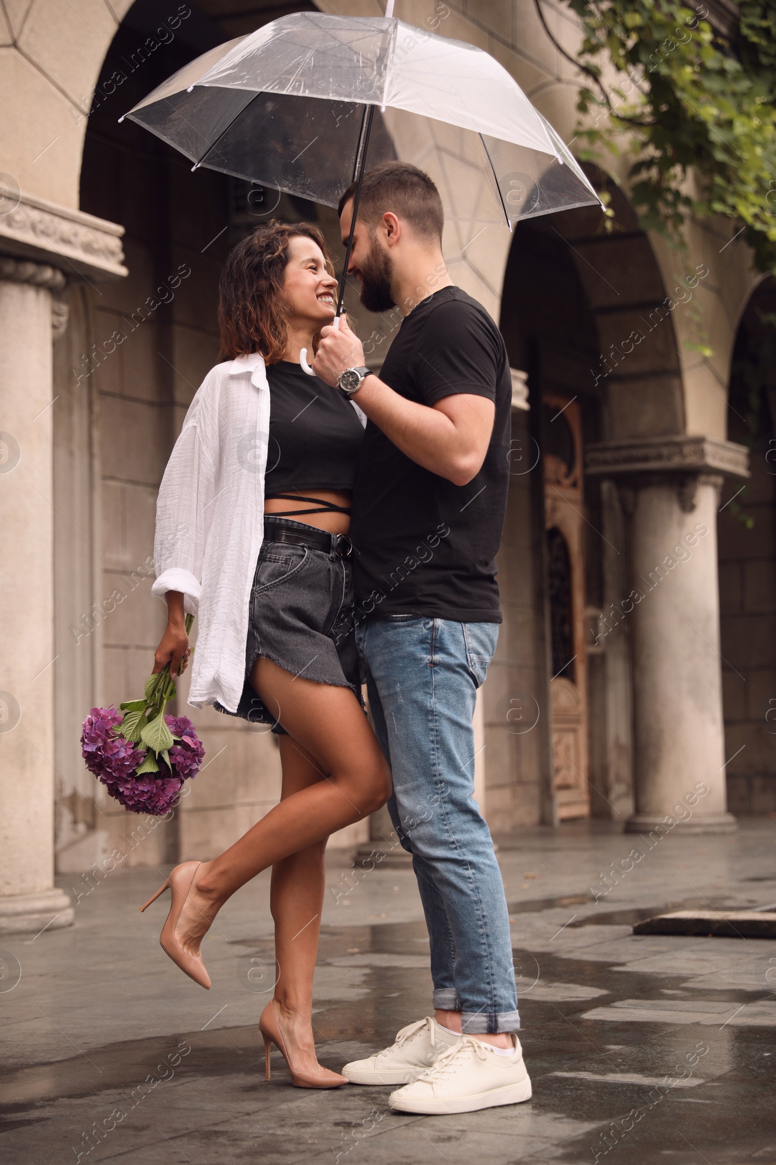 Photo of Young couple with umbrella enjoying time together under rain on city street