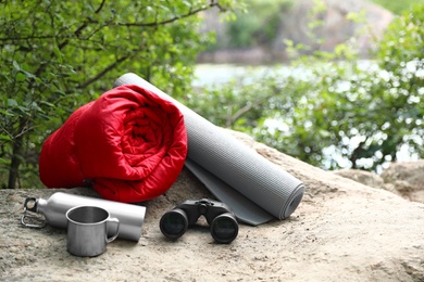 Photo of Rolled sleeping bag and other camping equipment on rock. Space for text