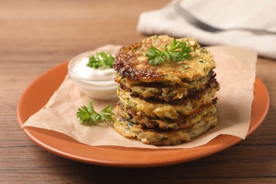 Photo of Delicious zucchini pancakes and bowl with sour cream on wooden table