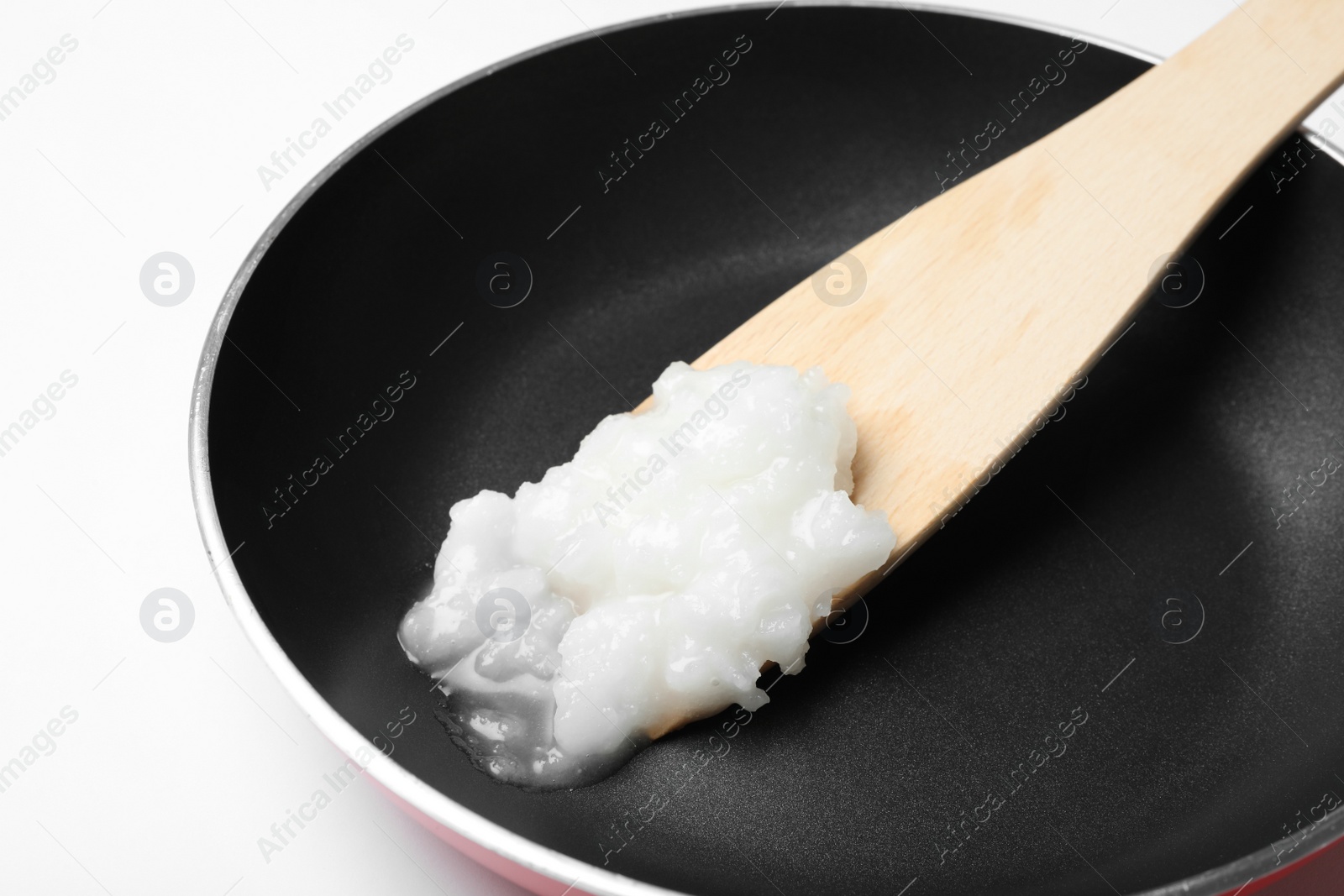 Photo of Frying pan with coconut oil and wooden spatula on white background, closeup. Healthy cooking