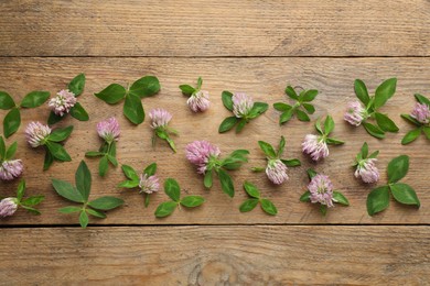 Photo of Beautiful clover flowers with green leaves on wooden background, flat lay