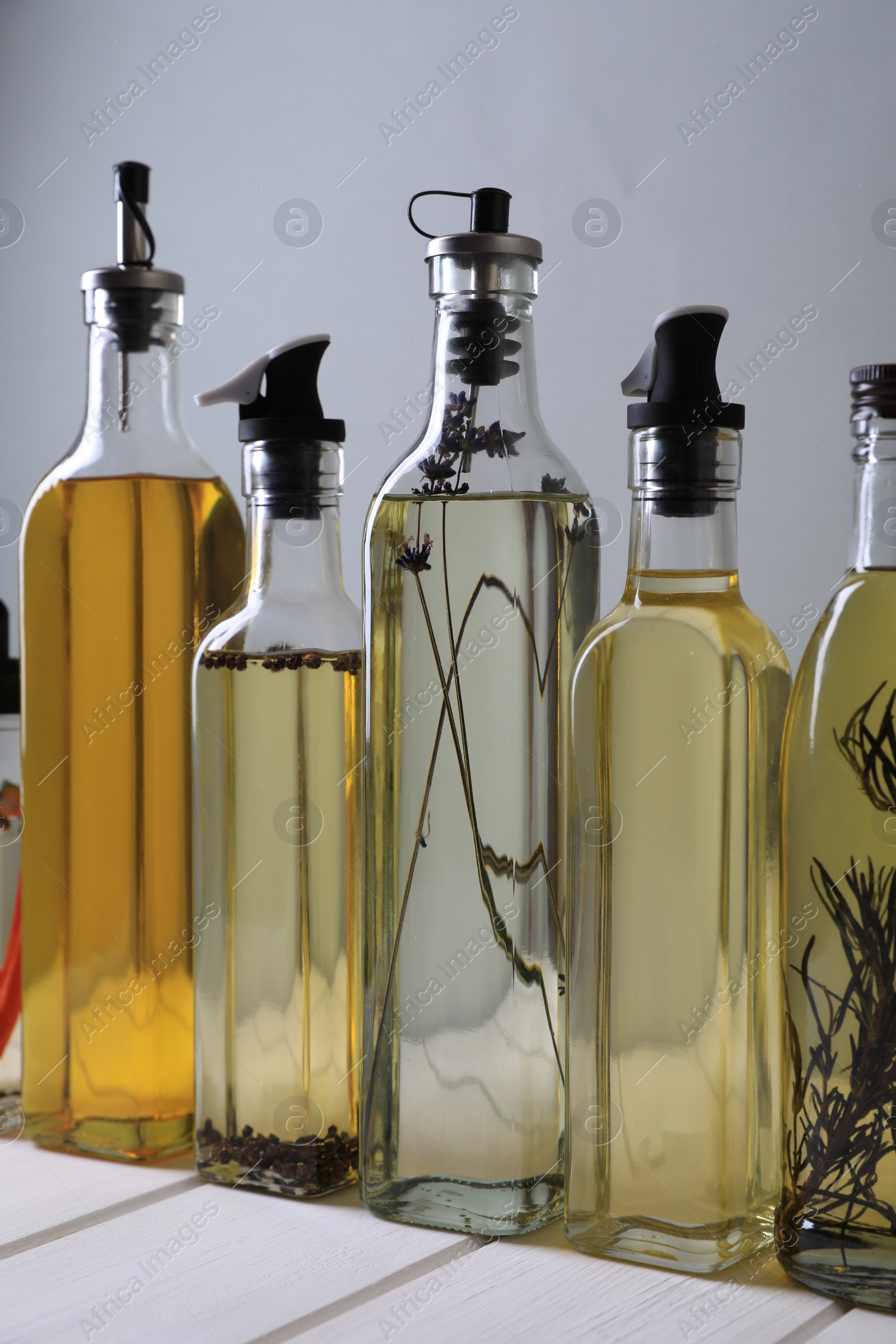 Photo of Bottles of different cooking oils on white wooden table against grey background
