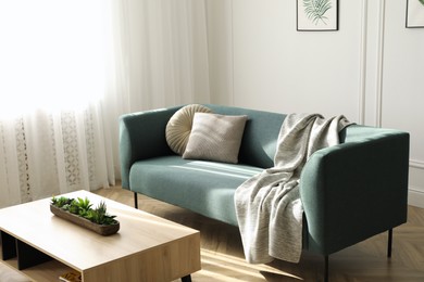Photo of Soft green sofa and wooden table in living room. Interior design