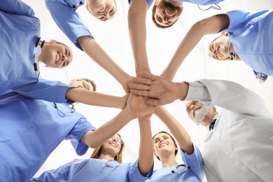 Doctor and interns stacking hands together against white background, bottom view