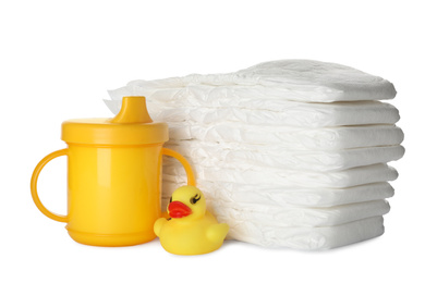Photo of Disposable diapers, toy duck and sippy cup on white background