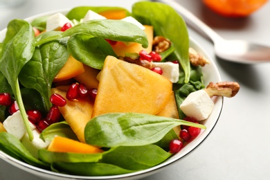 Delicious persimmon salad with pomegranate and spinach on light table, closeup