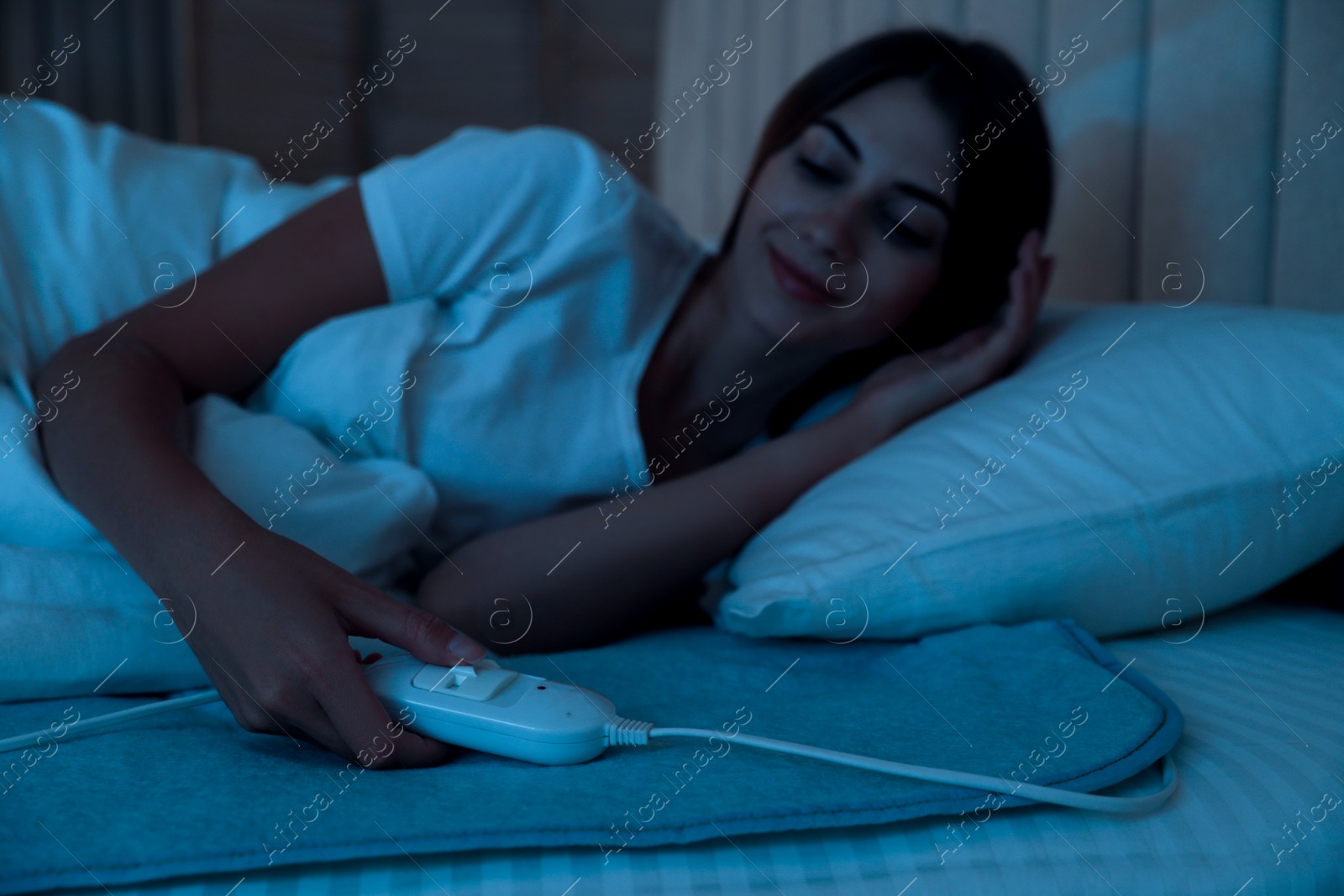 Photo of Young woman in bed with electric heating pad, focus on cable