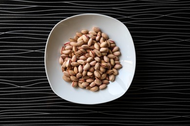 Photo of Many tasty pistachios on black table, top view